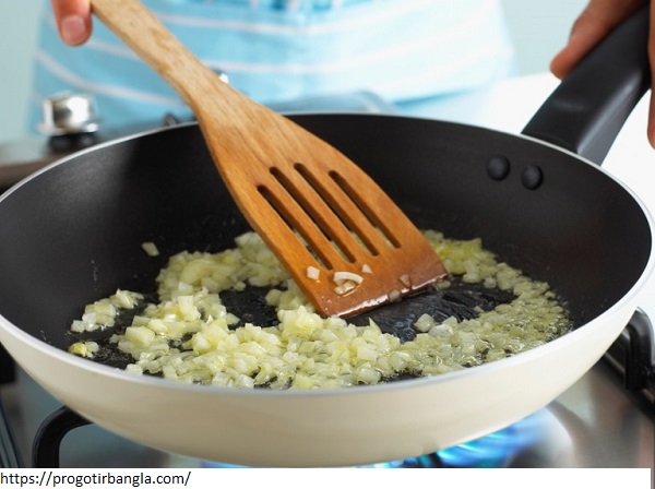 Child stirring chopped onions in frying pan using wooden spatula